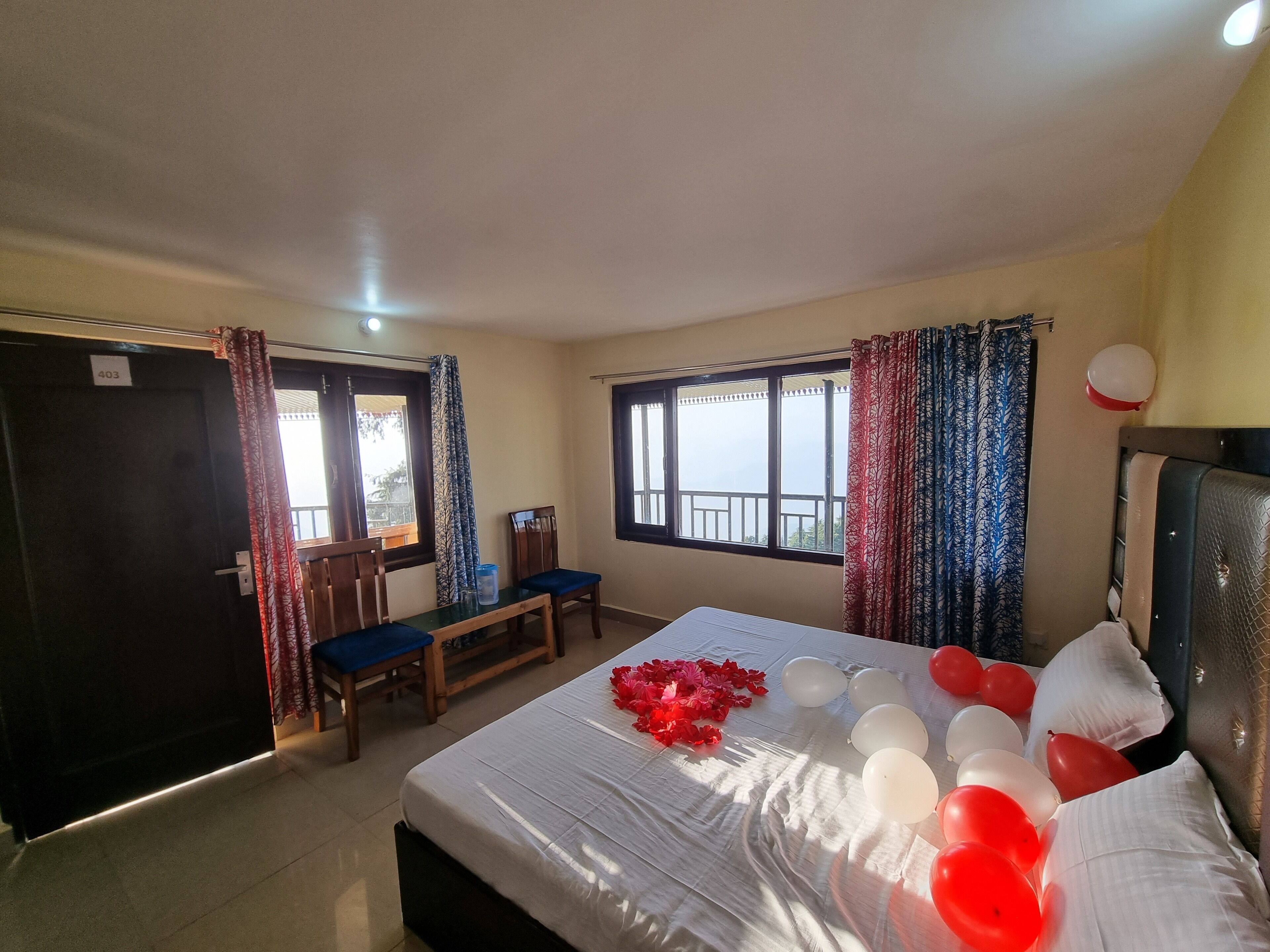 A hotel room with a bed, a desk, and a chair. There are curtains on the windows, and a balloon is visible on the wall.