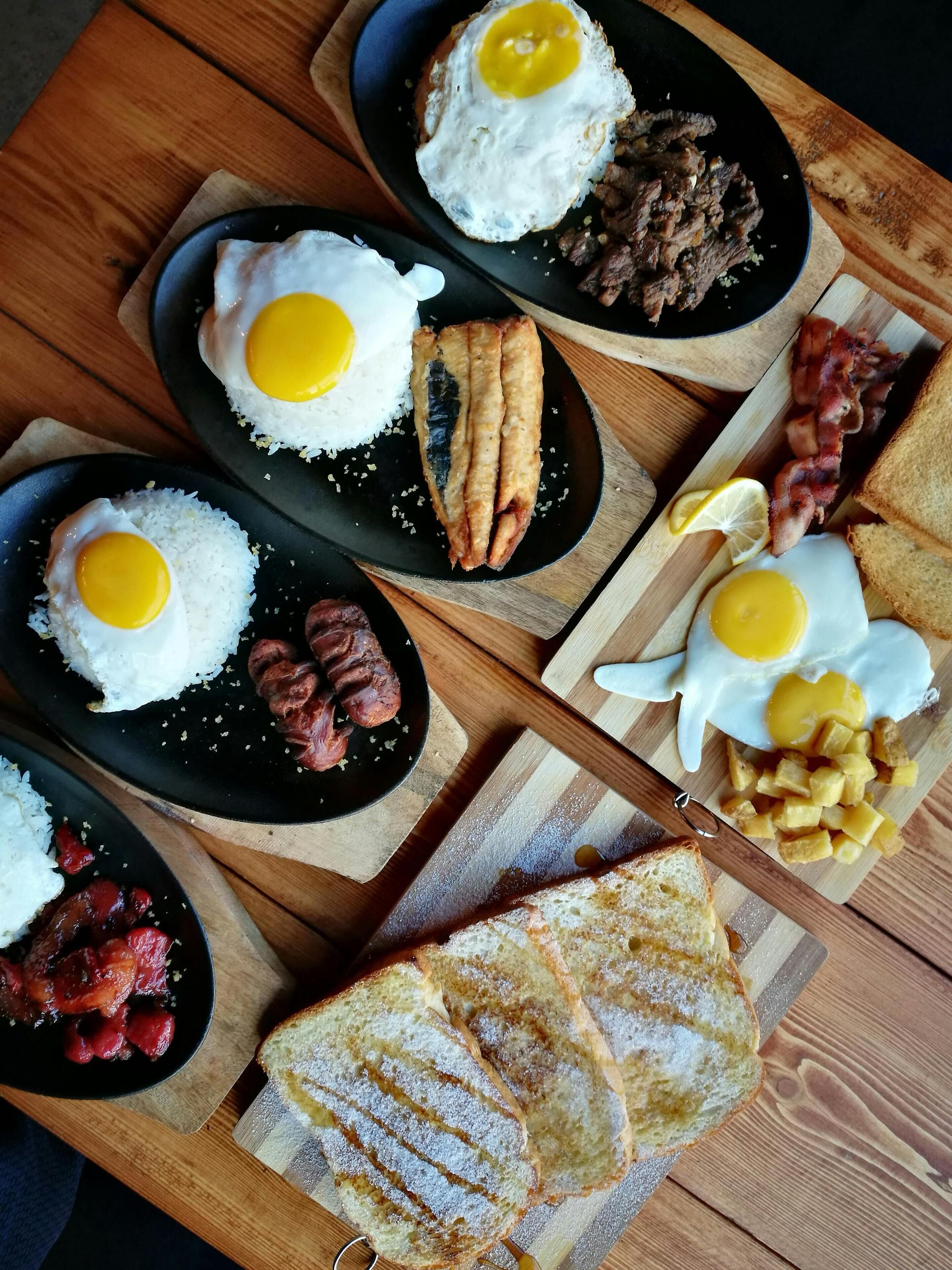 Una mesa de madera con una bandeja de desayuno que incluye huevos, salchichas, tocino, tostadas y fruta.