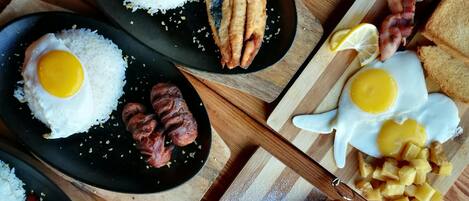 Una mesa de madera con una bandeja de desayuno que incluye huevos, salchichas, tocino, tostadas y fruta.