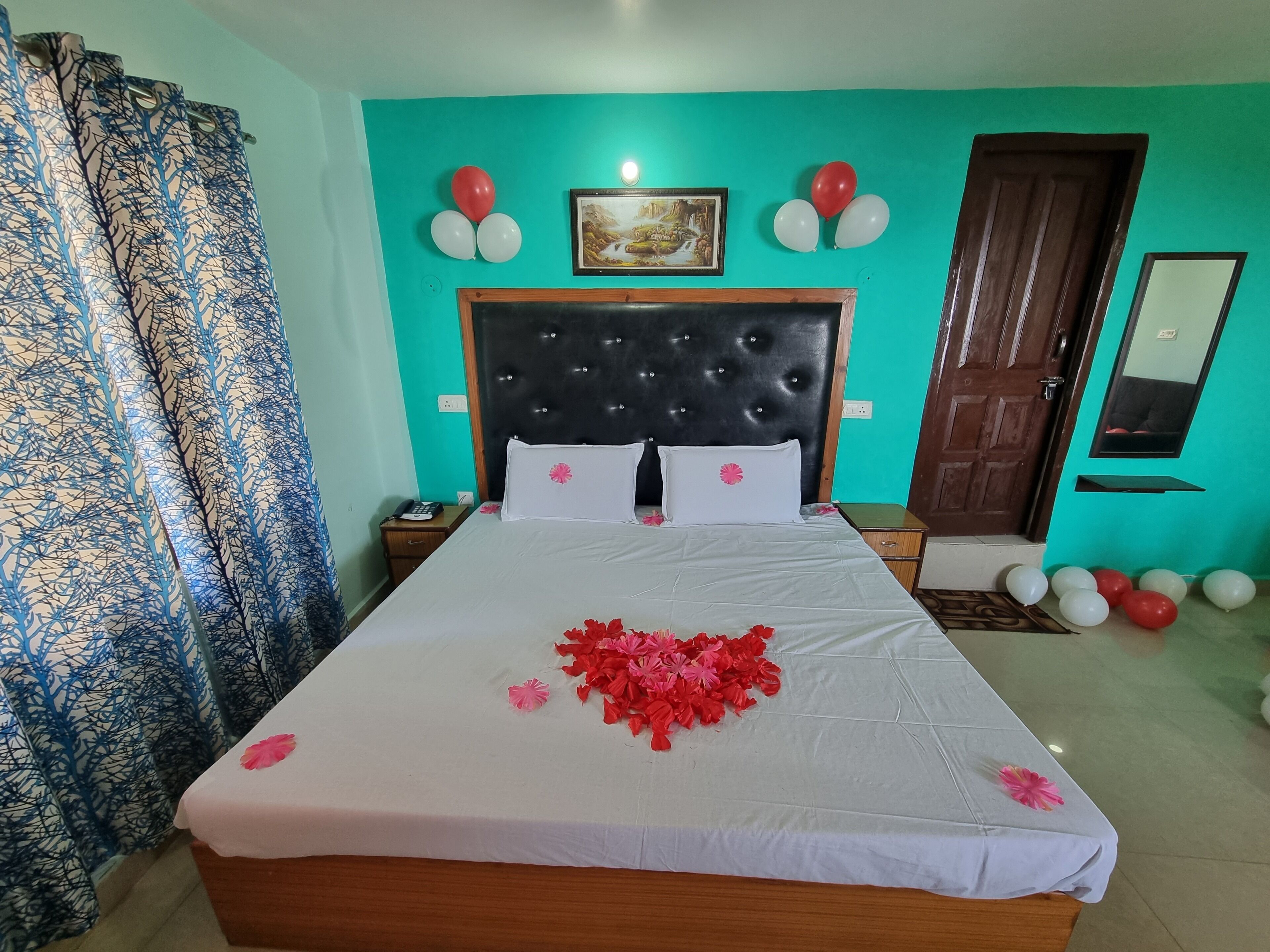 Une chambre avec un grand lit, des murs de couleur turquoise, une tête de lit noire et des ballons.