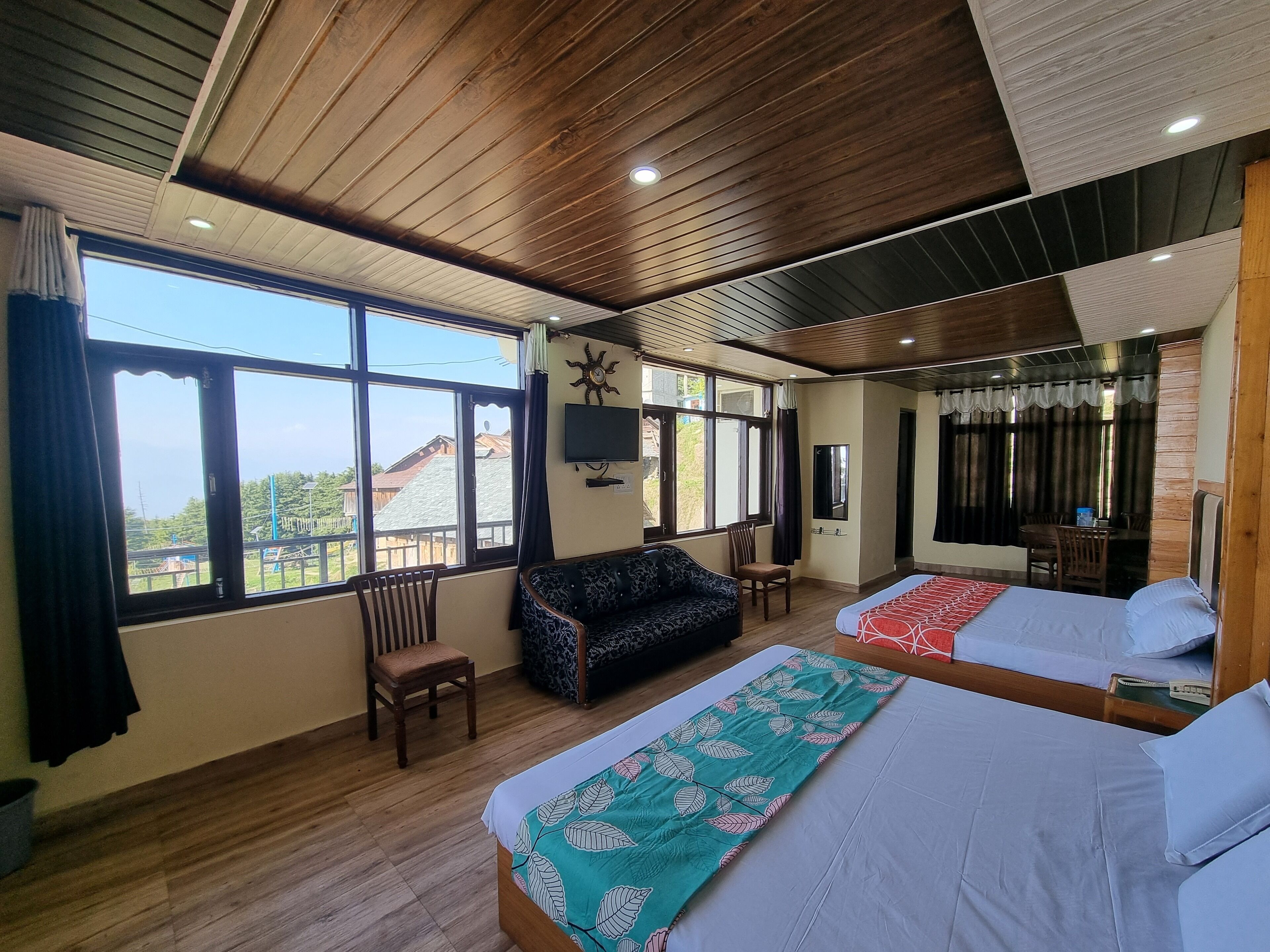 A hotel room with two beds, a sofa, a TV, and large windows offering a view of the outside.
