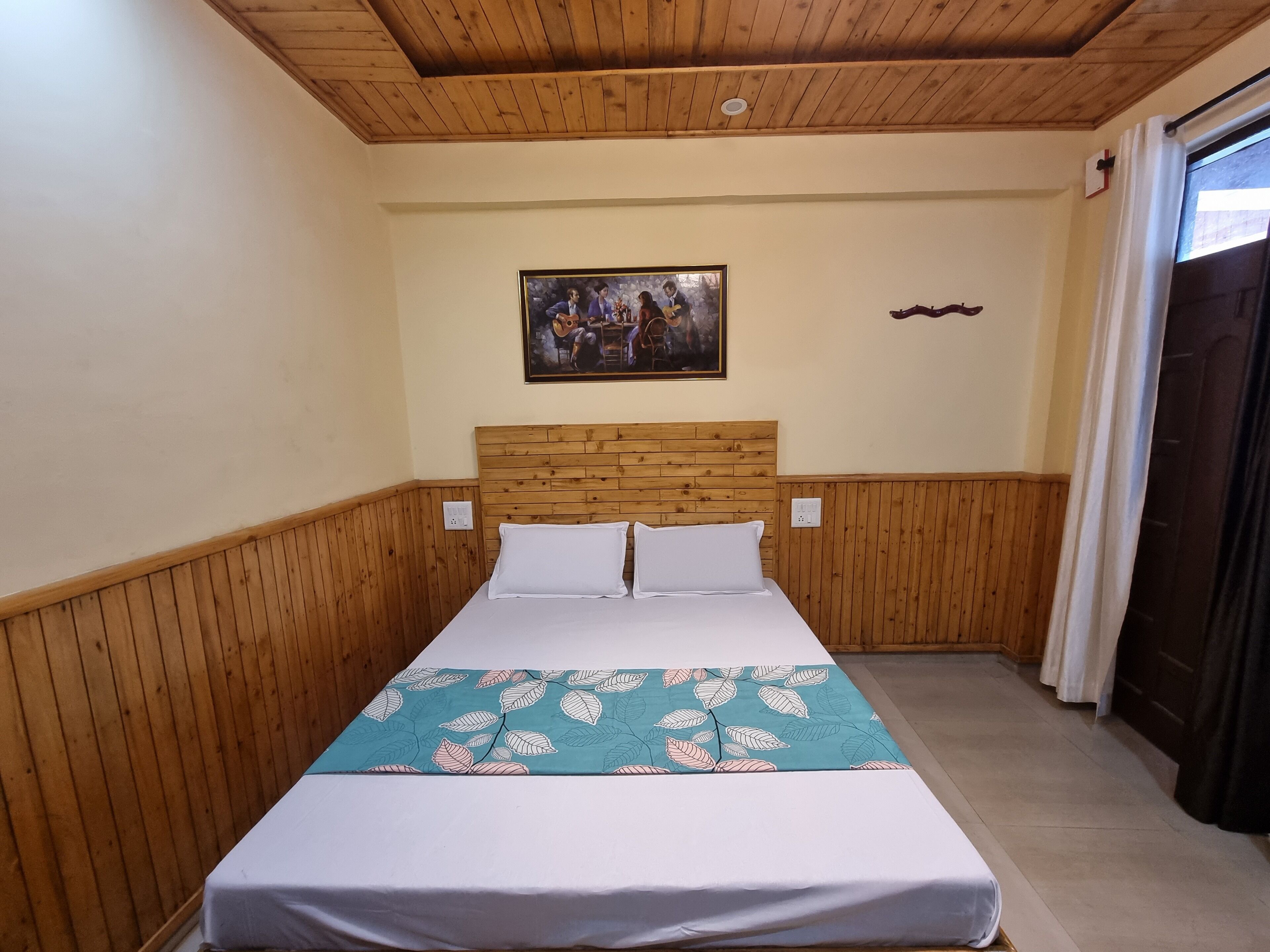 Een kamer met een bed met houten hoofdbord, een schilderij aan de muur en een raam met gordijnen.