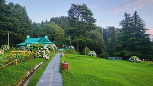 A stone pathway leading to a green-roofed building surrounded by lush greenery and trees. - Smart Hill Kalatop (Dalhousie)
