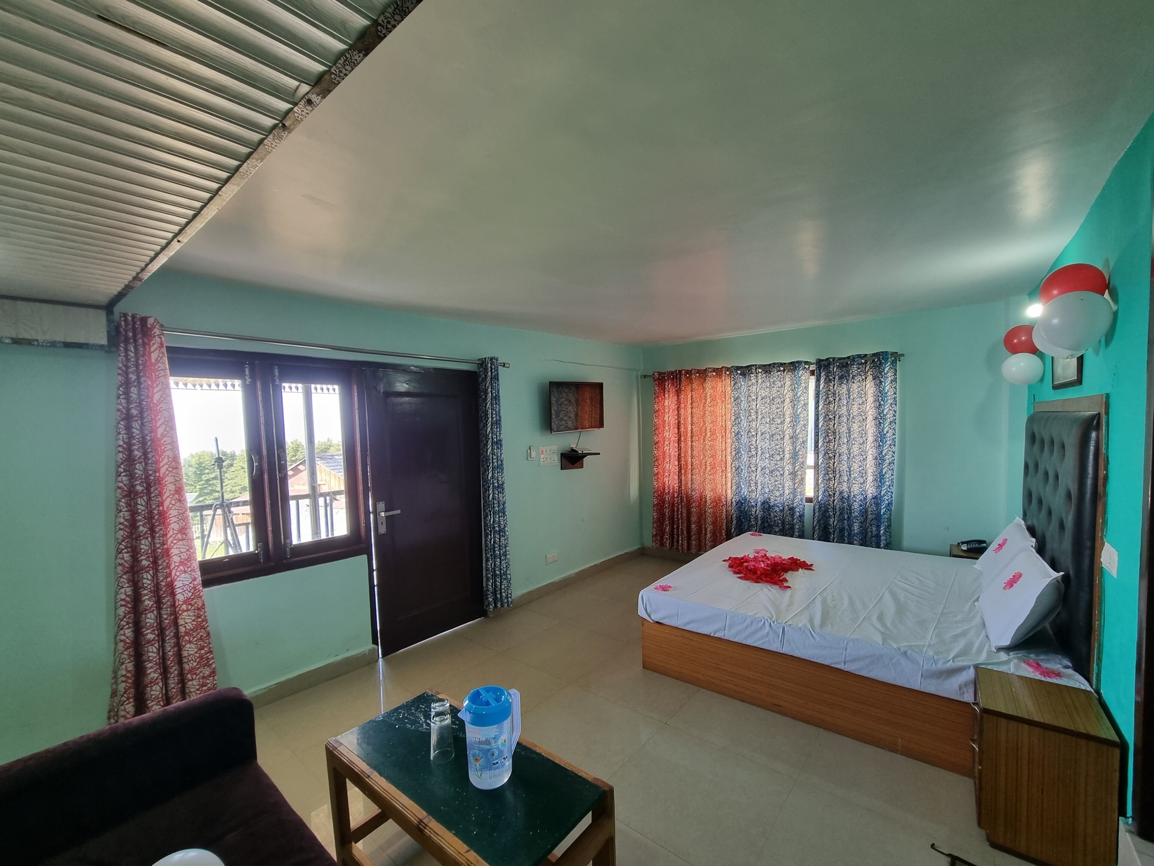 A hotel room with a bed, a table with a water bottle, a chair, a window with curtains, and a door.