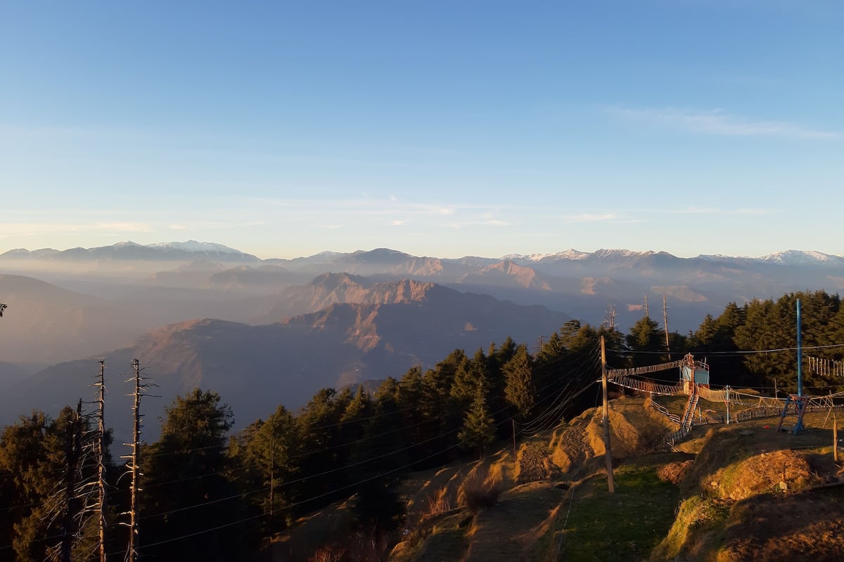A mountainous landscape with a clear sky. There are trees and a wooden structure on the right side.