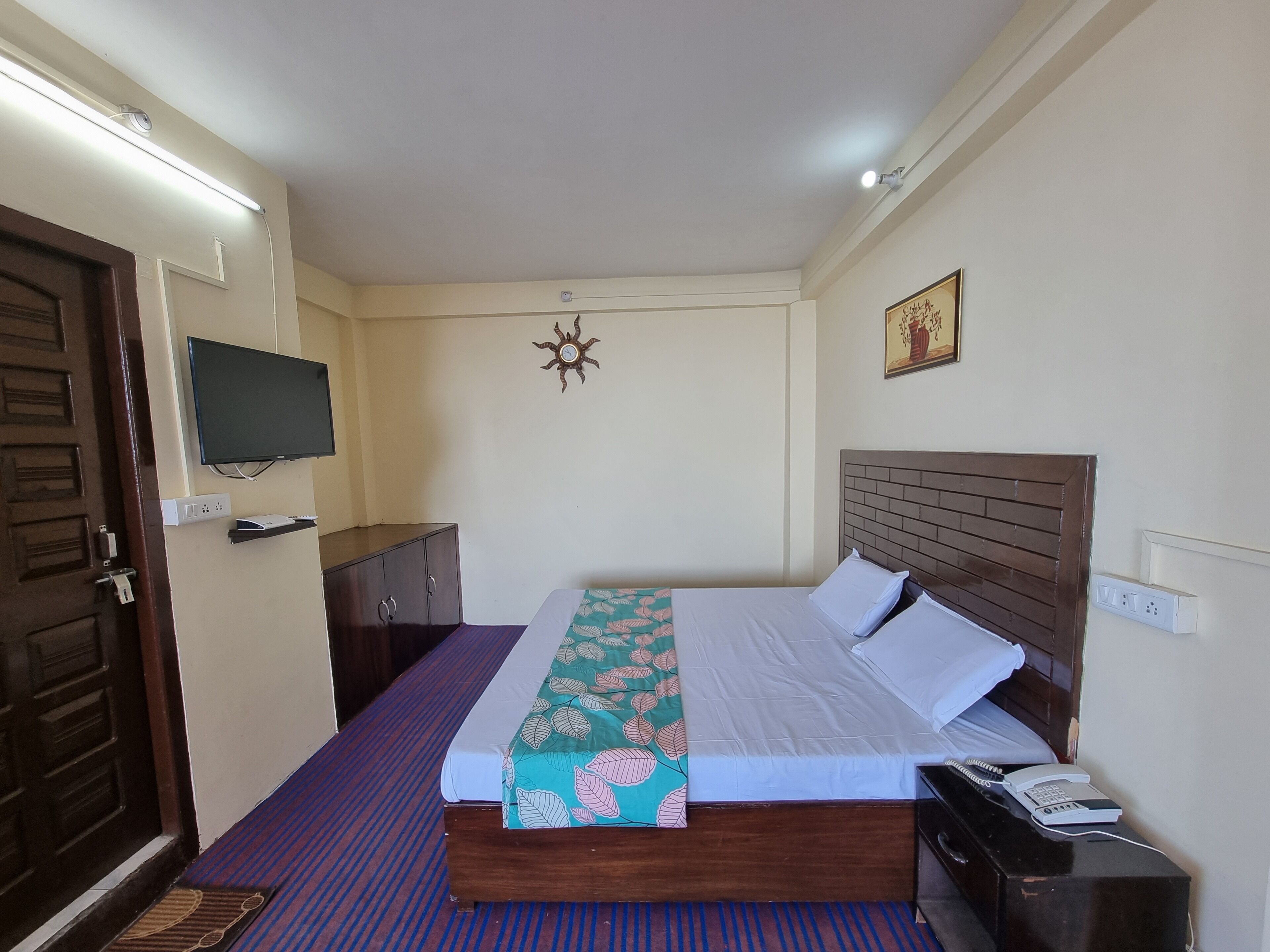 Une chambre à coucher comprenant un lit, un téléviseur fixé au mur, une armoire et une table de chevet avec un téléphone.