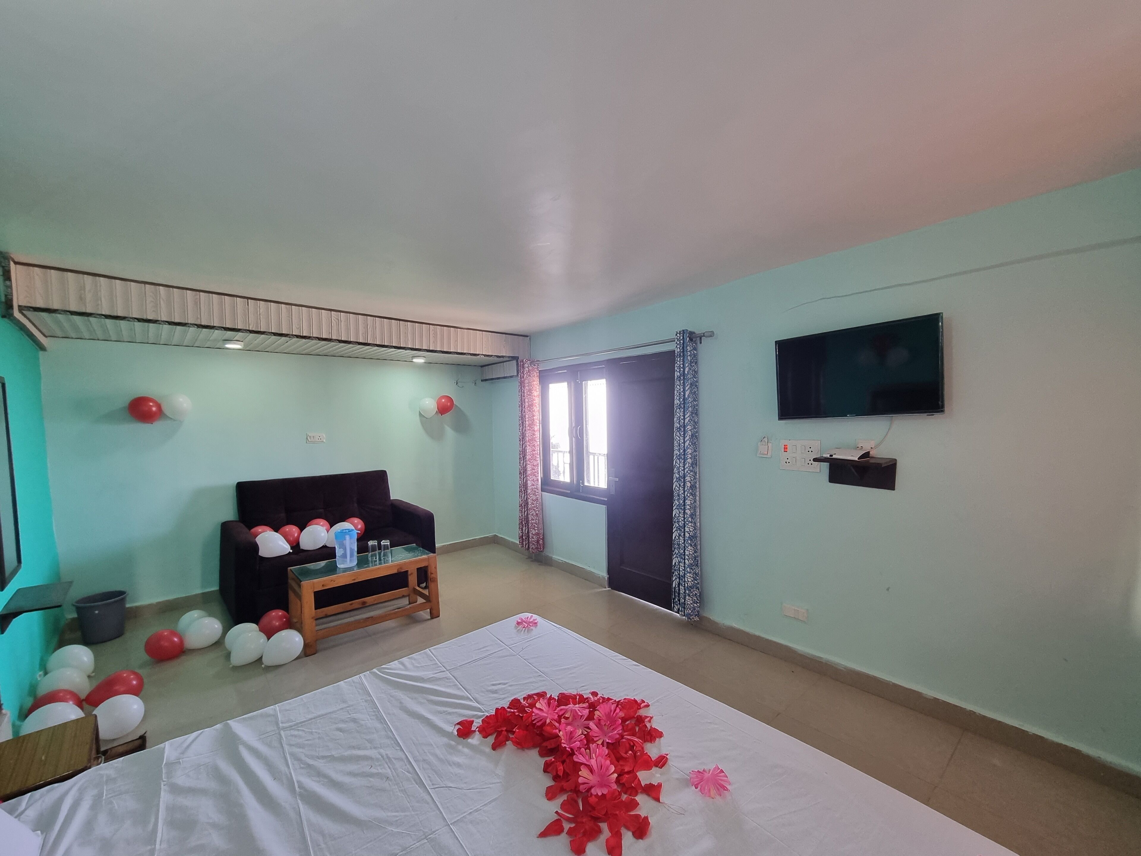Une pièce aux murs de couleur turquoise, avec un canapé noir, une table décorée de ballons et un téléviseur fixé au mur.