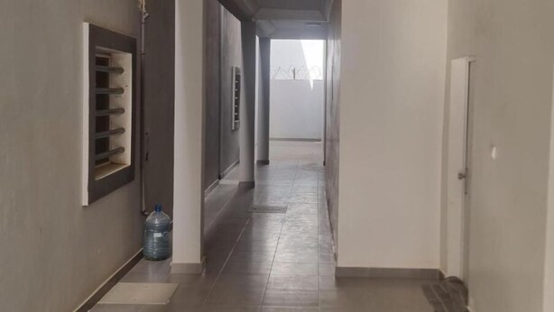 Een gang met een waterdispenser, een prullenbak en een deur aan het einde.