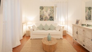 A living room with a white sofa, two lamps, a wooden coffee table with a vase, a white cabinet, and a painting on the wall. - Campo Viola 10 people (Rome)