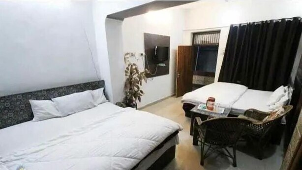 Habitación de hotel con dos camas, una mesita, una silla, un televisor y una ventana con cortinas.
