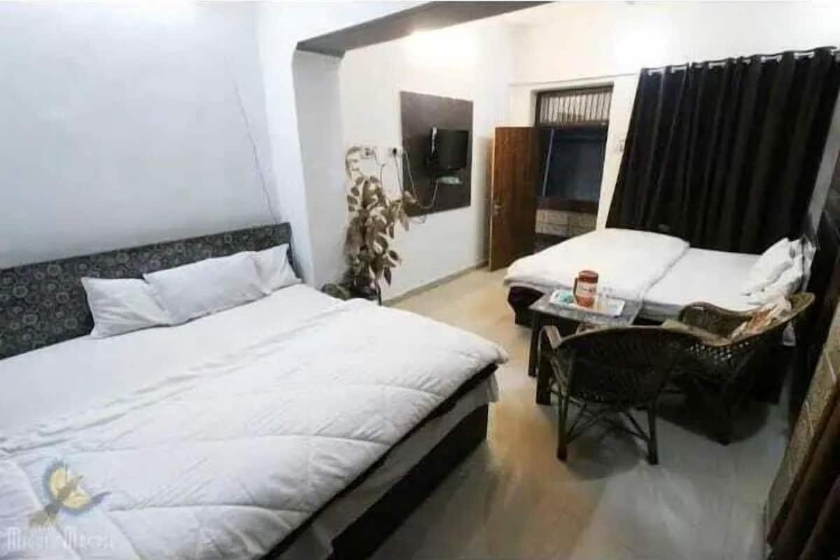 A hotel room with two beds, a small table, a chair, a TV, and a window with curtains.