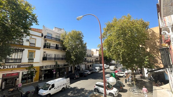A street view with parked cars, a white van, and buildings with balconies and signage. - Panther Home Adriano (Seville)