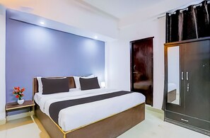 A modern hotel room with a large bed, a wardrobe, and a nightstand with a vase of flowers.
