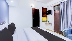Ein modernes Hotelzimmer mit einem Bett, einem Schreibtisch, einem Sessel, einem Fernseher und einem Fenster mit Vorhängen.