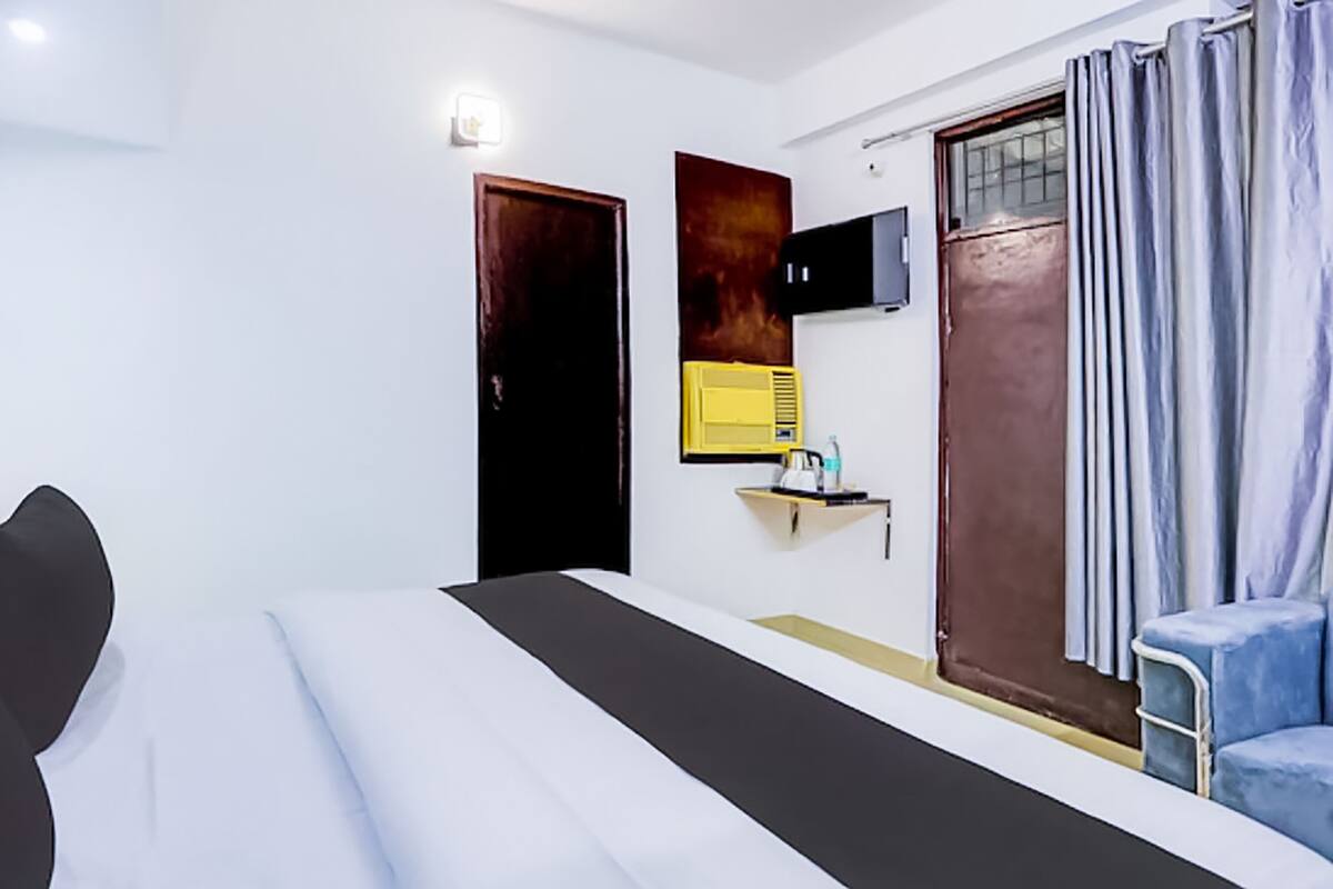 A modern hotel room with a bed, a desk, a chair, a TV, and a window with curtains.