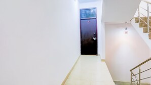 Un passadís estret amb una porta al final, una escala a la dreta i una làmpada penjant a dalt.