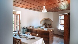 A rustic kitchen with a wooden ceiling, a stone archway, and a dining table set with white tablecloths. - Melody House in Roustika (Rethymno)