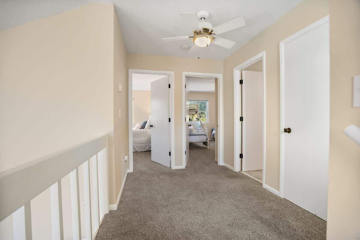 A hallway with carpeted floors, white walls, and a ceiling fan.