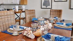 Una mesa de comedor dispuesta con sillas de mimbre, cristalería y una variedad de conchas marinas.