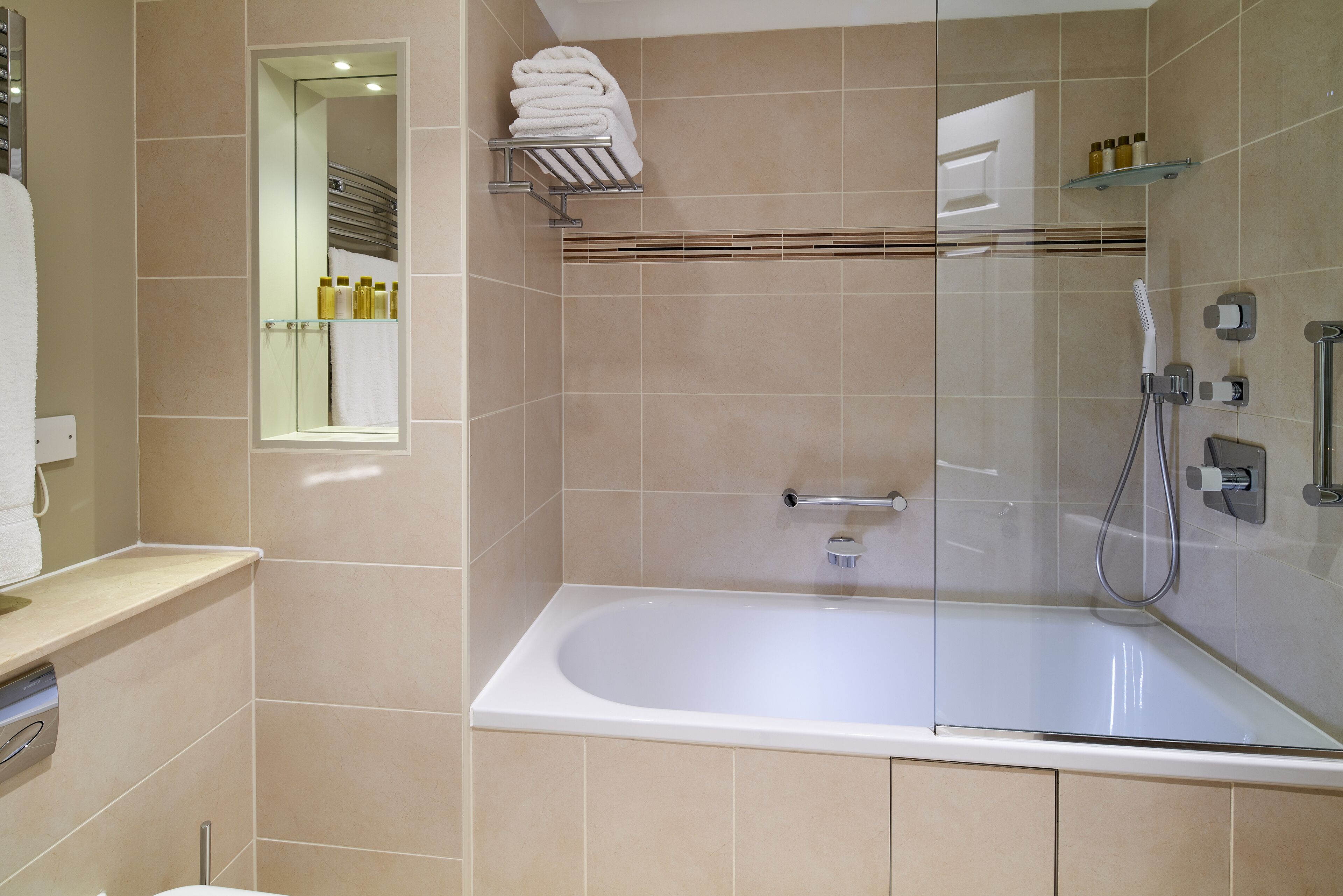 A modern bathroom with a glass-enclosed shower, a white bathtub, and a mirror with a towel rack above it.