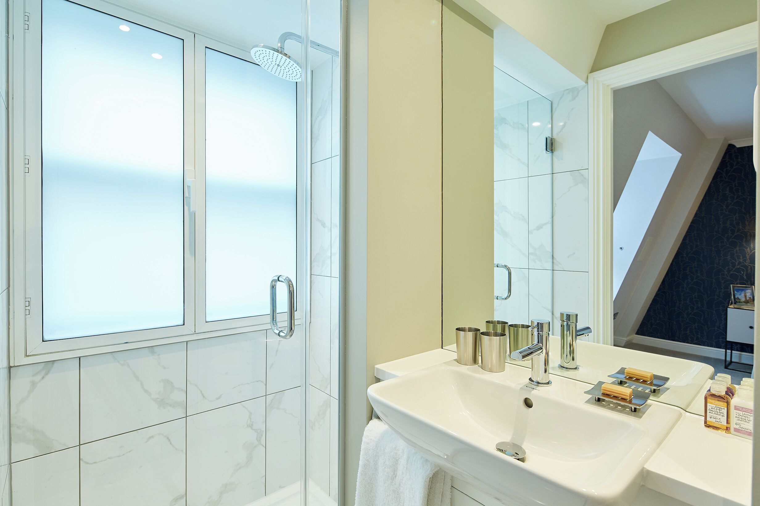 A modern bathroom with a glass shower enclosure, a white sink with two soap dispensers, and a large mirror.
