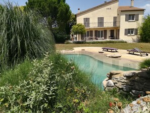 A pool area with lounge chairs, a stone wall, and a building with balconies in the background. - 3 bedroom private vacation home in cavaillon (Cavaillon)