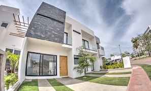 A modern two-story house with a flat roof, large windows, and a well-maintained lawn.