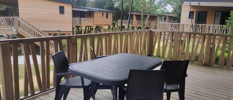 Una terraza de madera con una mesa y sillas, rodeada por un cerco de madera y edificios de madera al fondo.