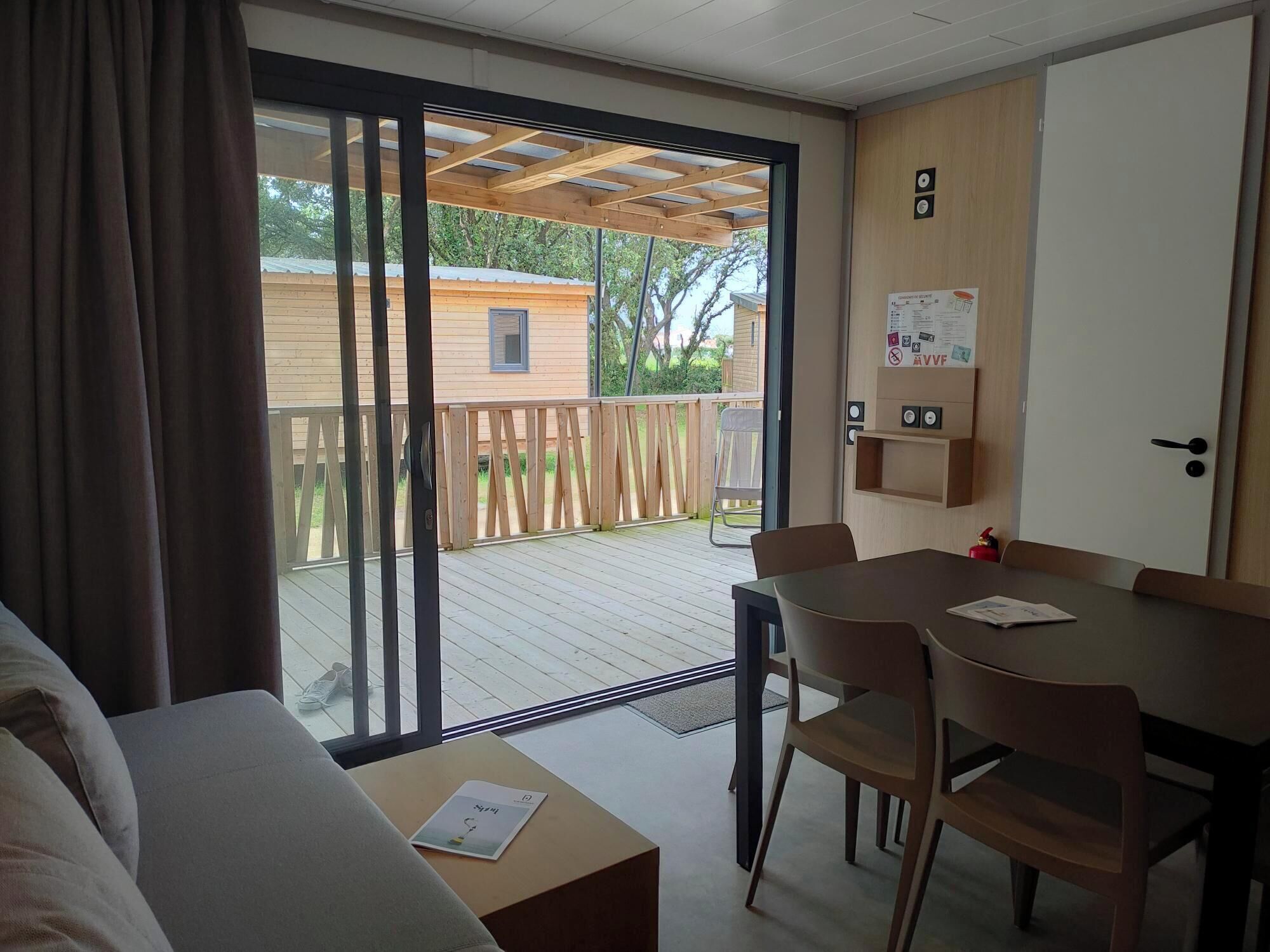 A room with a sliding glass door leading to a wooden deck, a small table with chairs, and a bed.
