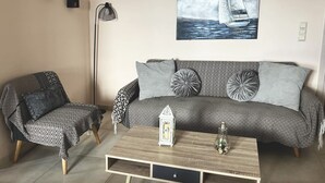 Un salon avec un canapé à motifs, un fauteuil à motifs, une table basse en bois, un lampadaire et un tableau représentant un voilier, accroché au mur.