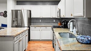 Una cocina moderna con armarios blancos, electrodomésticos de acero inoxidable, encimeras de granito y piso de madera.
