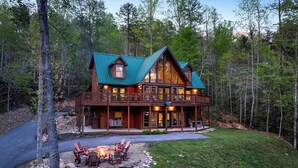 A large log cabin with a green roof, multiple balconies, and a fire pit area. - Upscale 4 Bedroom Amazing View, Hot Tub, Arcade/Theater, No Winding Roads! (Sevierville)