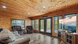 A cozy cabin interior with a wooden ceiling, a large TV, and a couch. - Upscale 4 Bedroom Amazing View, Hot Tub, Arcade/Theater, No Winding Roads! (Sevierville)