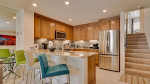 A modern kitchen with wooden cabinets, stainless steel appliances, and a marble island with bar stools.