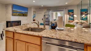 A modern kitchen with granite countertops, stainless steel appliances, wooden cabinets, and a large window with a view of a lake.