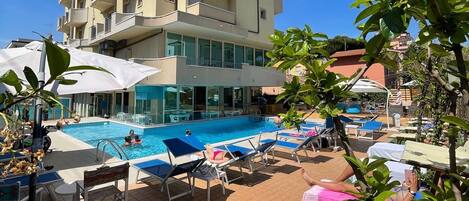 A pool area with lounge chairs and umbrellas, surrounded by a building with balconies.