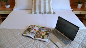 A neatly made bed with a striped pillow, a laptop, and a magazine on a quilted bedspread. - Hotel Apogeo  (Rimini)