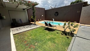 A backyard with a swimming pool, a lawn, and a patio area with seating.