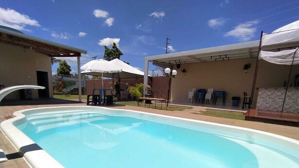 A swimming pool with a tiled deck, surrounded by a covered patio area with umbrellas.