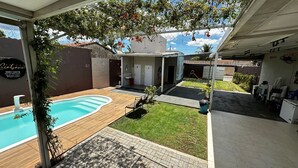 A backyard with a swimming pool, a small garden, and a covered patio area.
