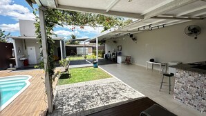 A covered outdoor area with a pool, a barbecue, and a patio with a table and chairs.