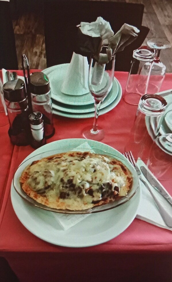 Una mesa preparada con una porción de pizza, una copa de vino y salsas.