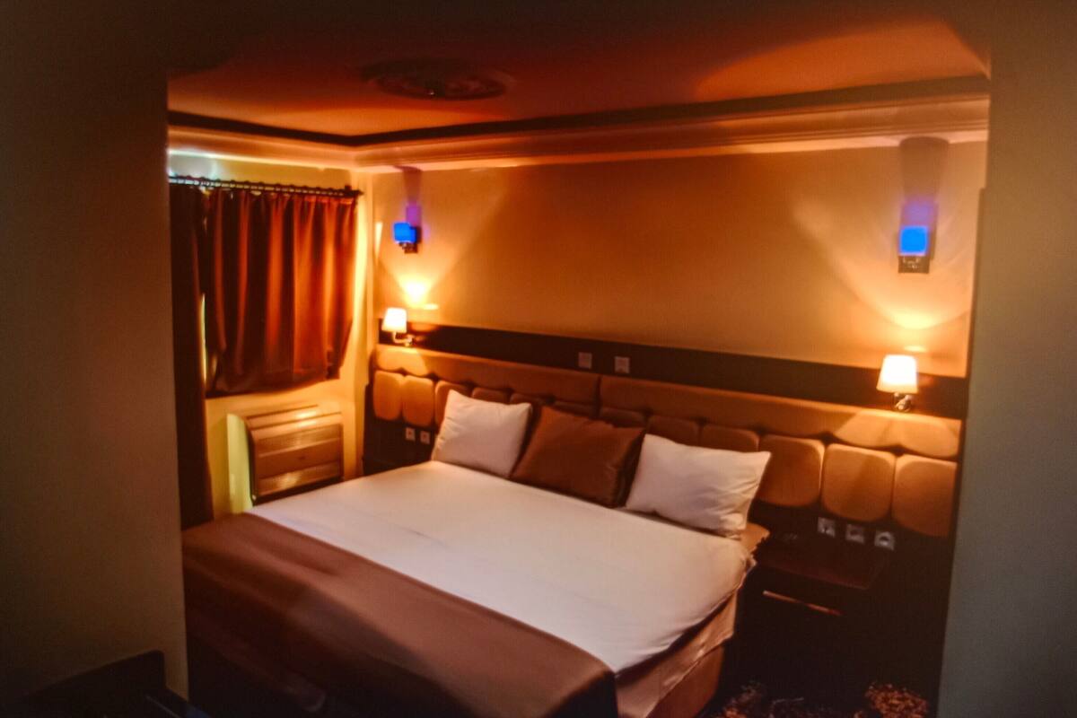 Habitación de hotel con una cama grande, dos lámparas de noche, cabecero con repisa incorporada y ventana con cortinas.