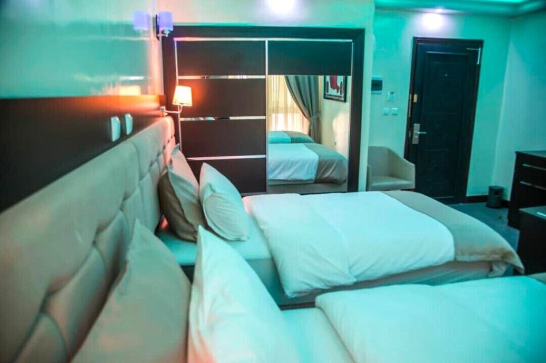 A hotel room with two beds, a sofa, a mirror, and a door leading to another room.