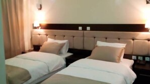 Ein Hotelzimmer mit zwei Betten, einem Kopfteil, Nachttischlampen und einer Deckenleuchte.