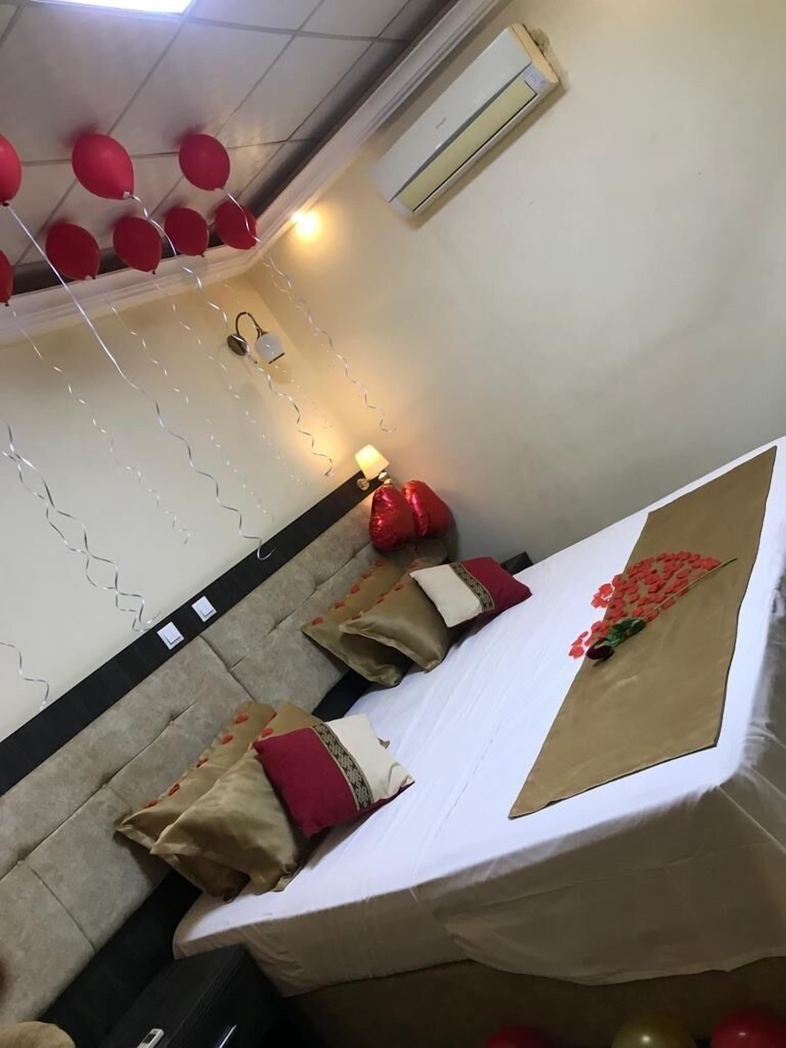 A hotel room with a bed, pillows, a bedside table, an air conditioner, and string lights.