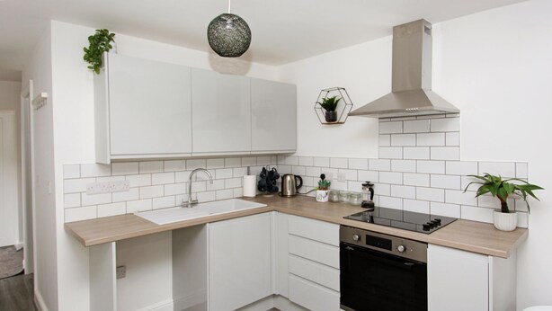 A modern kitchen with white cabinetry, a black stove, and a stainless steel range hood. - 3 bed detached house in Telford (Telford and Wrekin)