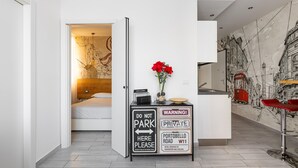 Ein modernes Hotelzimmer mit einem Bett, einem Schreibtisch mit einem Schild 'Bitte nicht parken', einer Vase mit roten Blumen und einem Wandgemälde einer Stadtansicht.