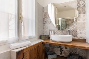 A bathroom with a large window, a white sink, a wooden vanity, and a decorative mirror. - Monterumici 36 - Saffi Glamorous Apartment (Bologna)