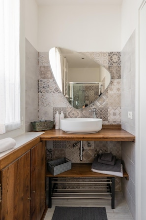 A bathroom with a wooden vanity, a white sink, a mirror, and patterned tiles. - Monterumici 36 - Saffi Glamorous Apartment (Bologna)